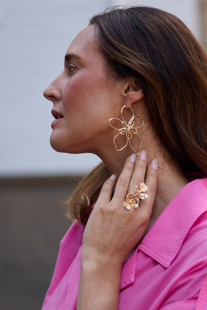 Woman wearing a pink shirt and gold jewelry outdoors