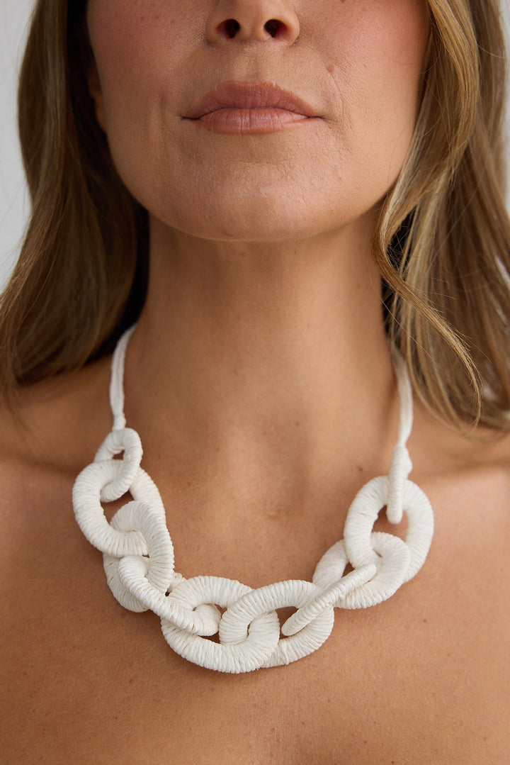 Woman wearing a white chain necklace against a plain background
