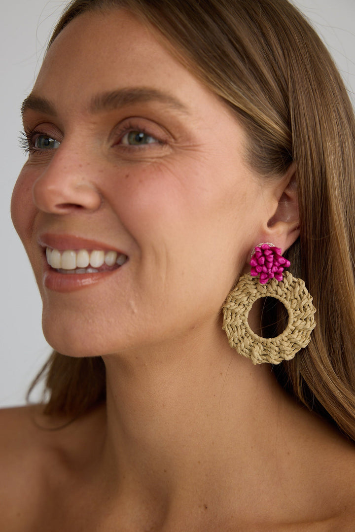 Woman wearing a large hoop earring with a pink flower detail on a plain background
