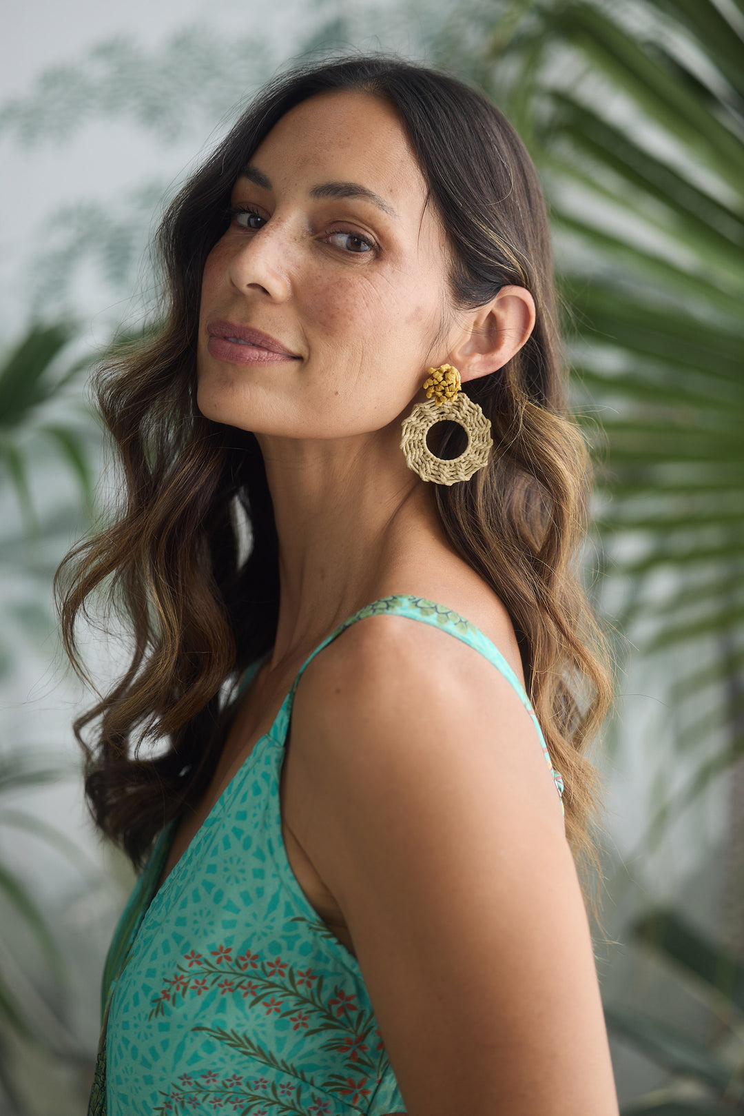 Woman wearing natural earrings with a green top against a blurred natural background