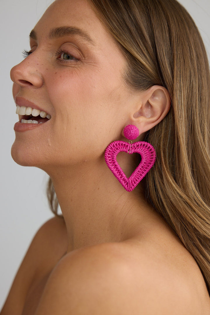 Woman wearing pink heart-shaped earrings against a plain background