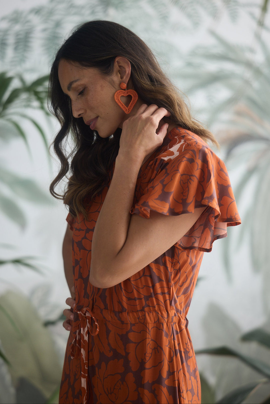 Woman wearing an orange patterned dress with heart-shaped earrings in a blurred indoor setting