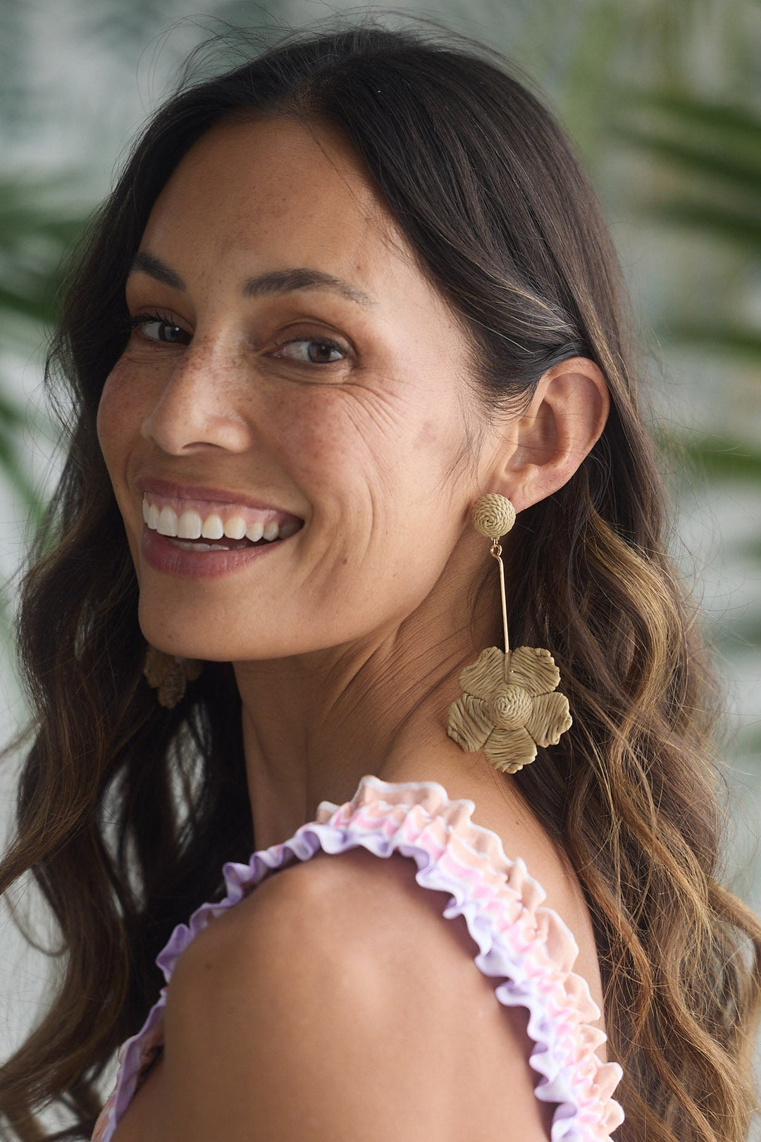 Woman wearing a colorful dress with ruffled sleeves against a leafy green background
