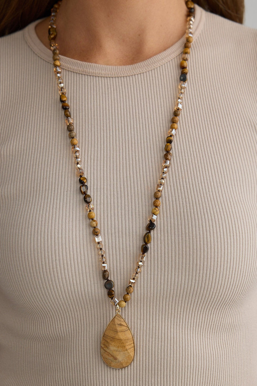 Person wearing a long beaded necklace with a pendant on a plain background