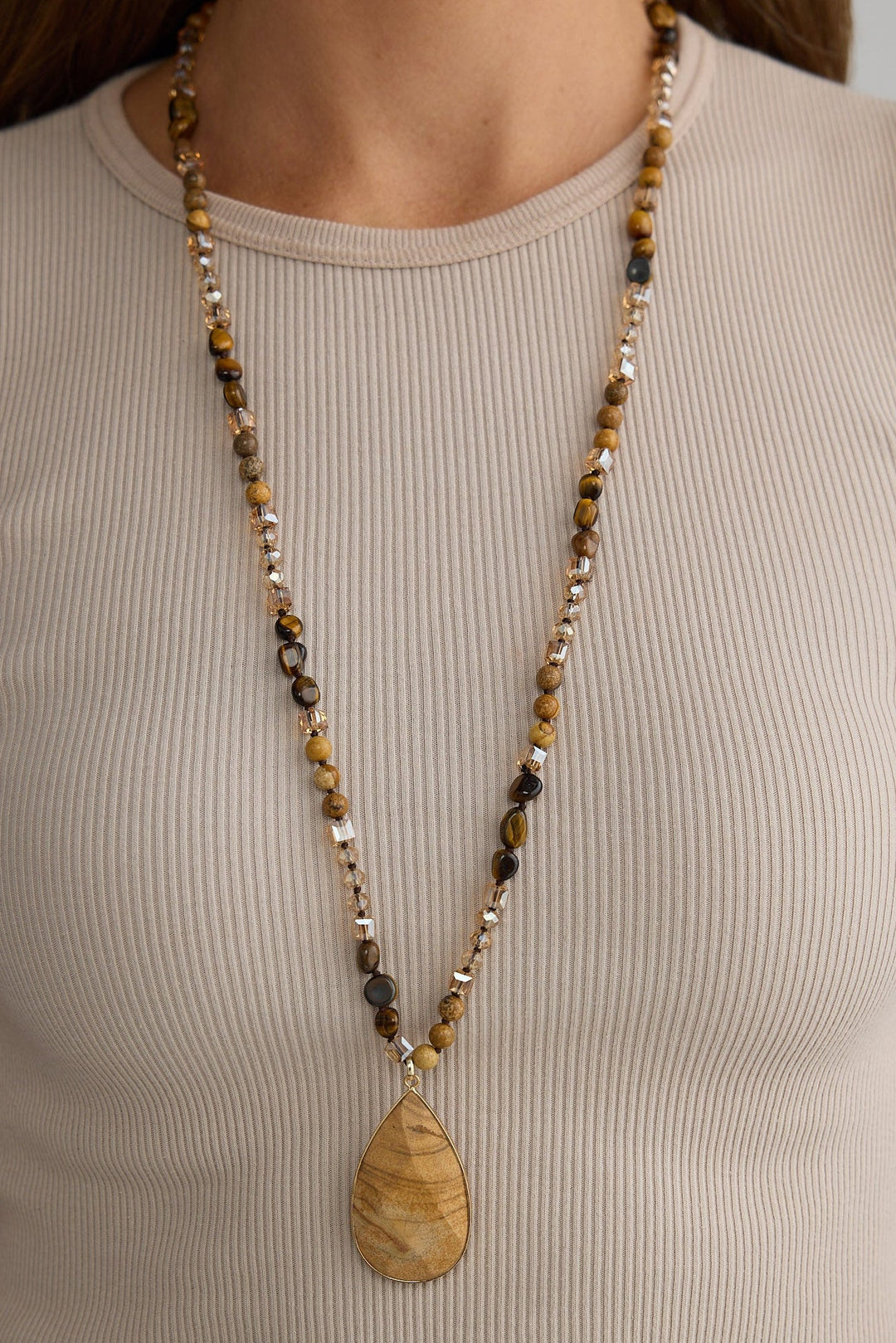 Person wearing a long beaded necklace with a pendant on a plain background