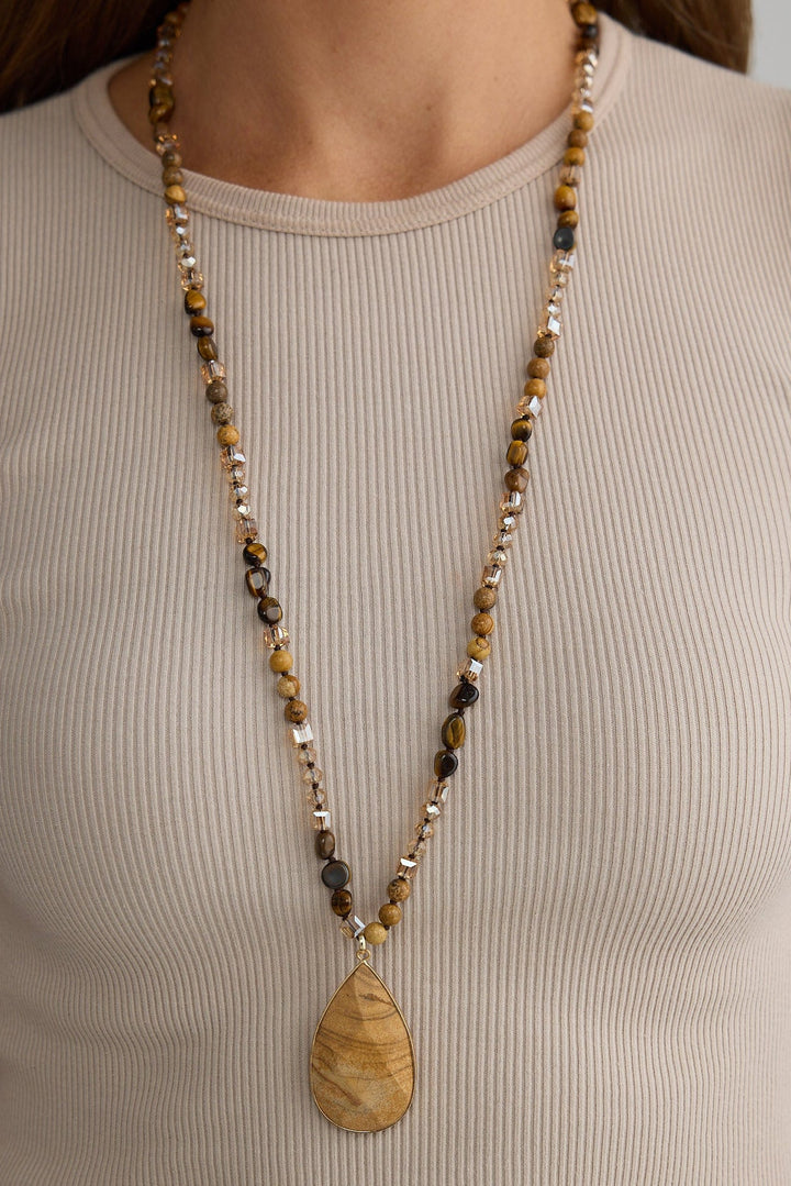 Person wearing a long beaded necklace with a pendant on a plain background