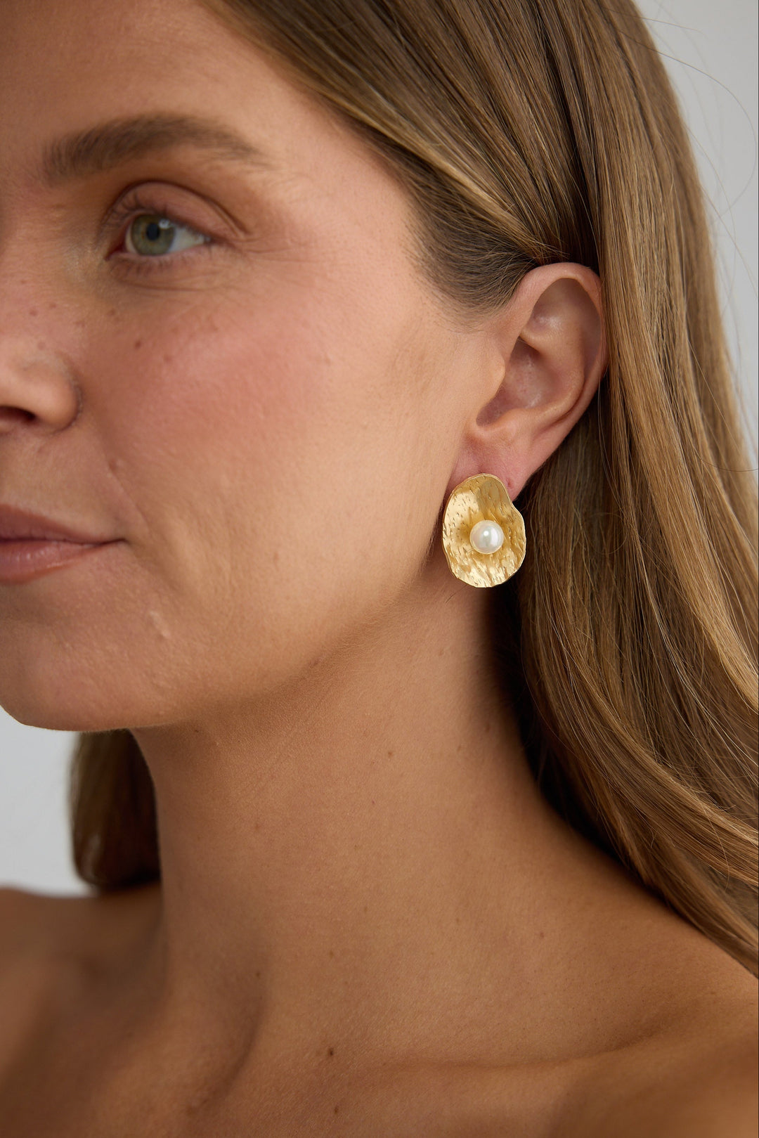 Close-up of a woman wearing gold earrings with a neutral background