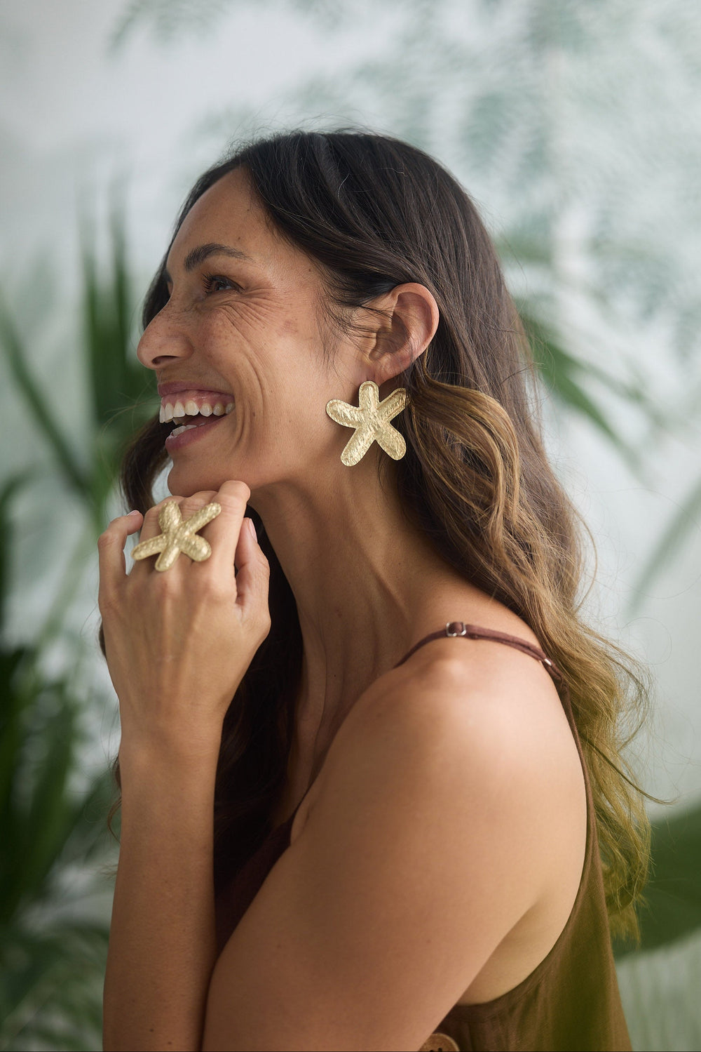 Woman wearing starfish shaped earrings and a ring, with a blurred green plant background