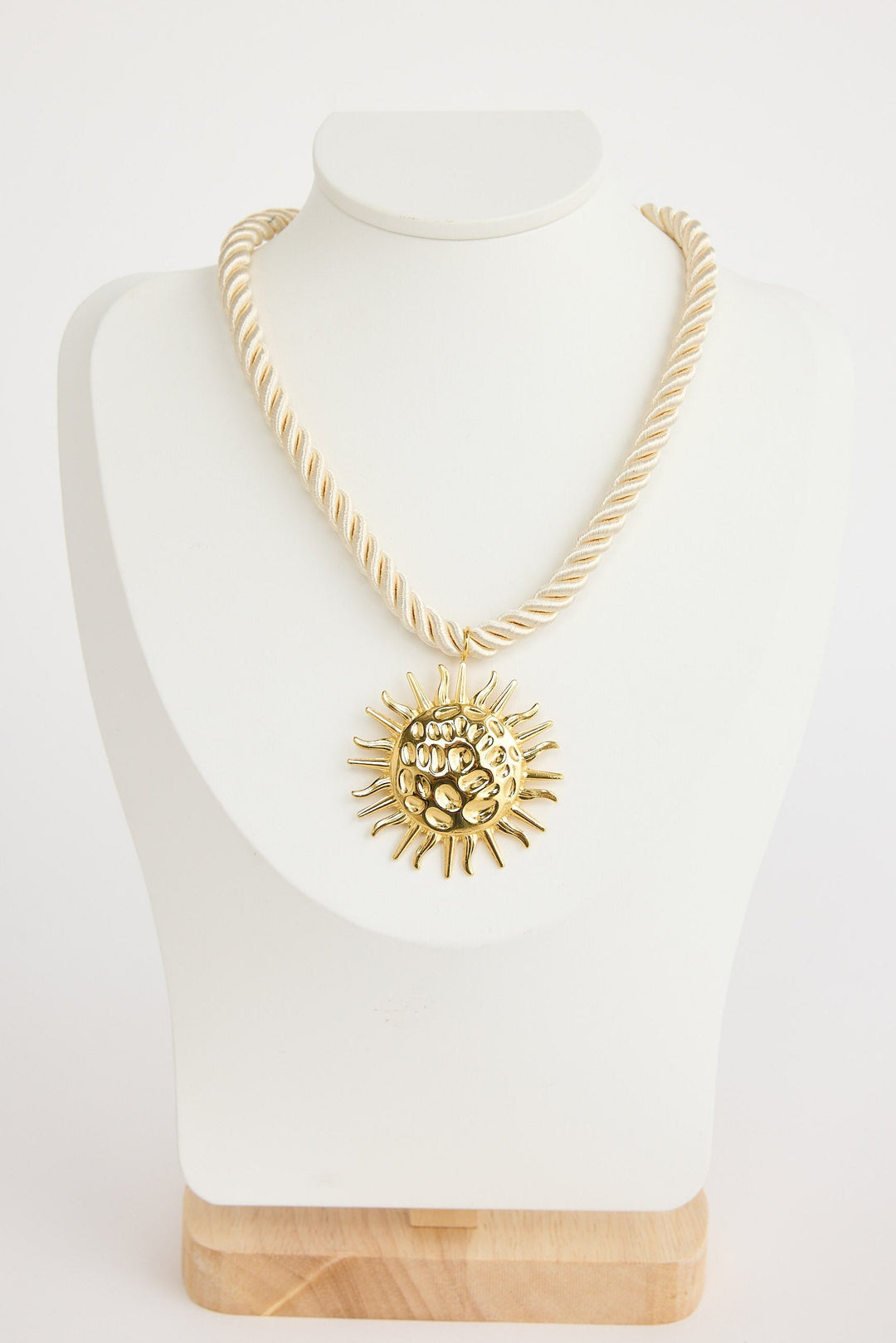 Gold necklace with a sun pendant on a mannequin bust against a white background