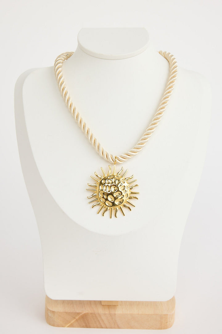 Gold necklace with a sun pendant on a mannequin bust against a white background