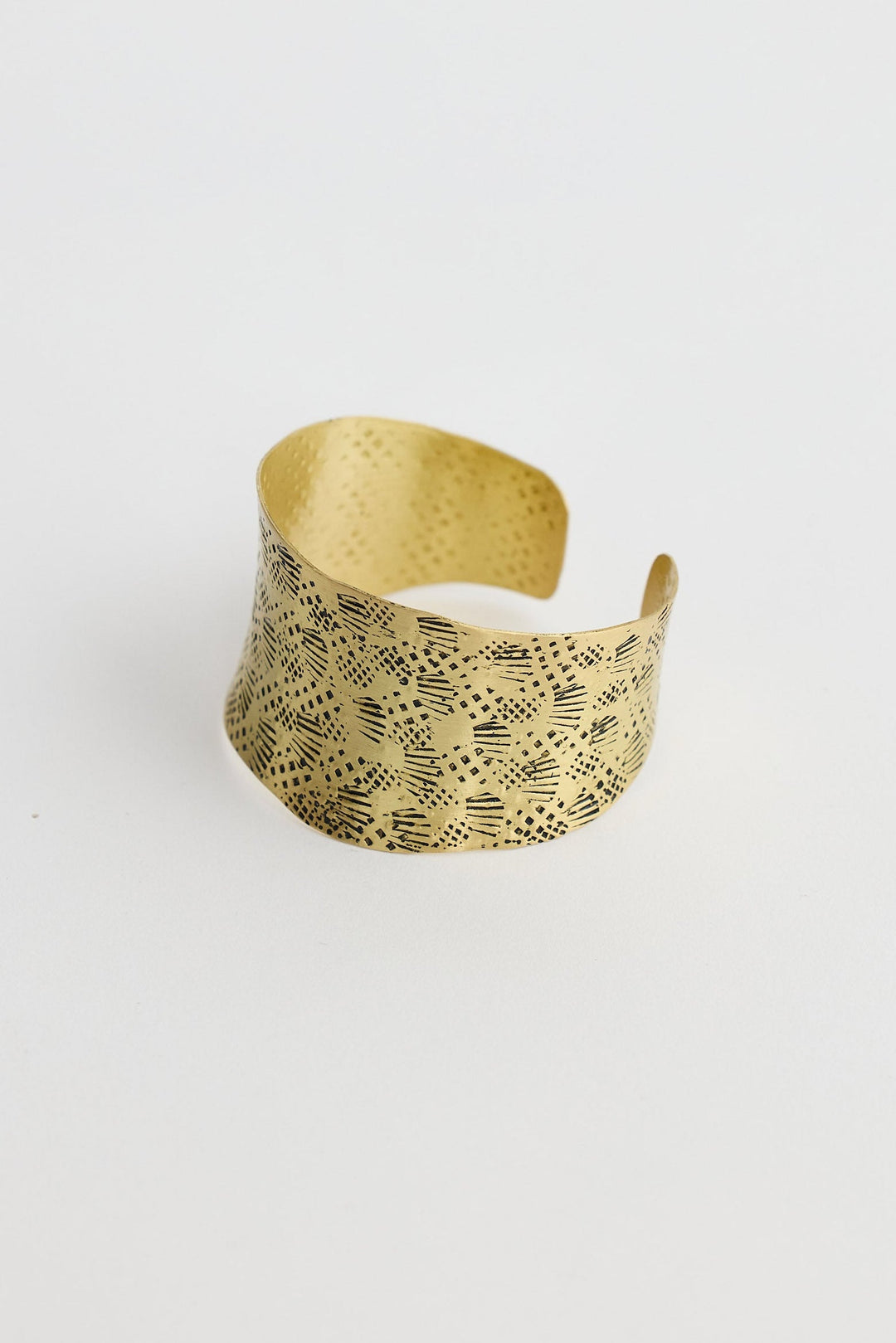 Gold cuff with a textured pattern on a white background