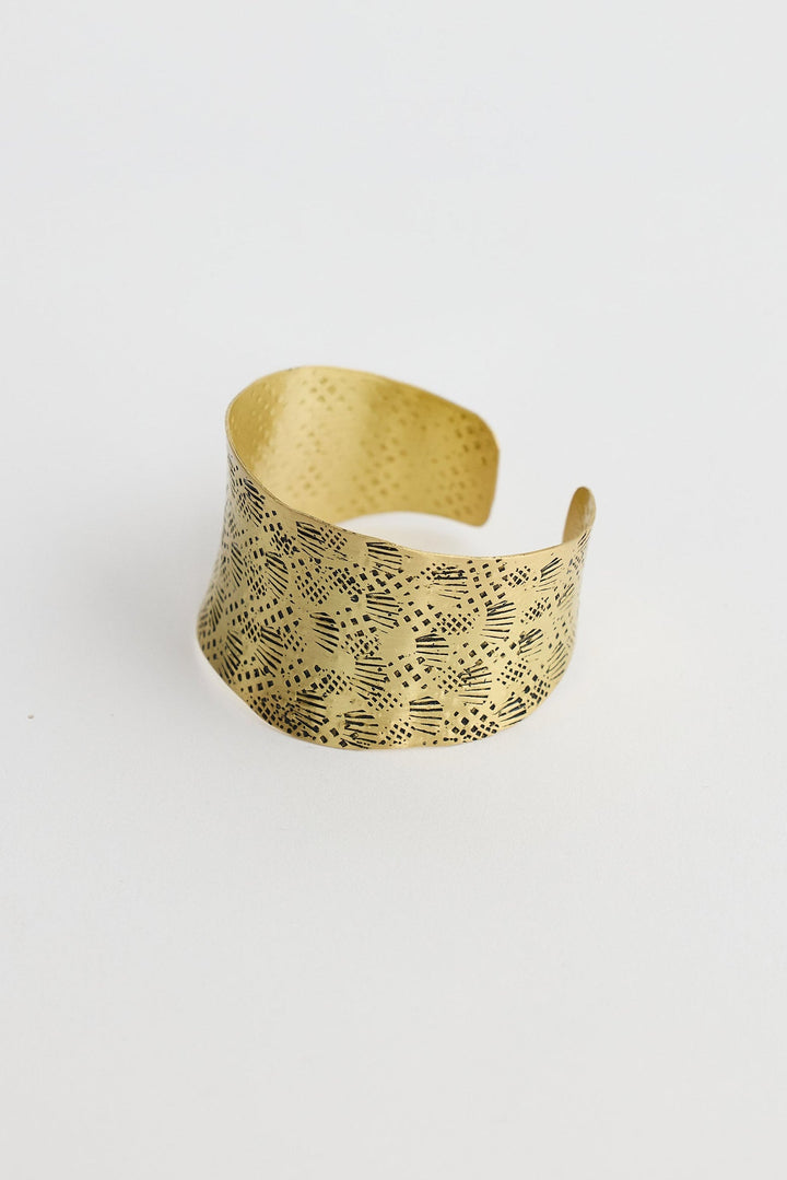 Gold cuff with a textured pattern on a white background