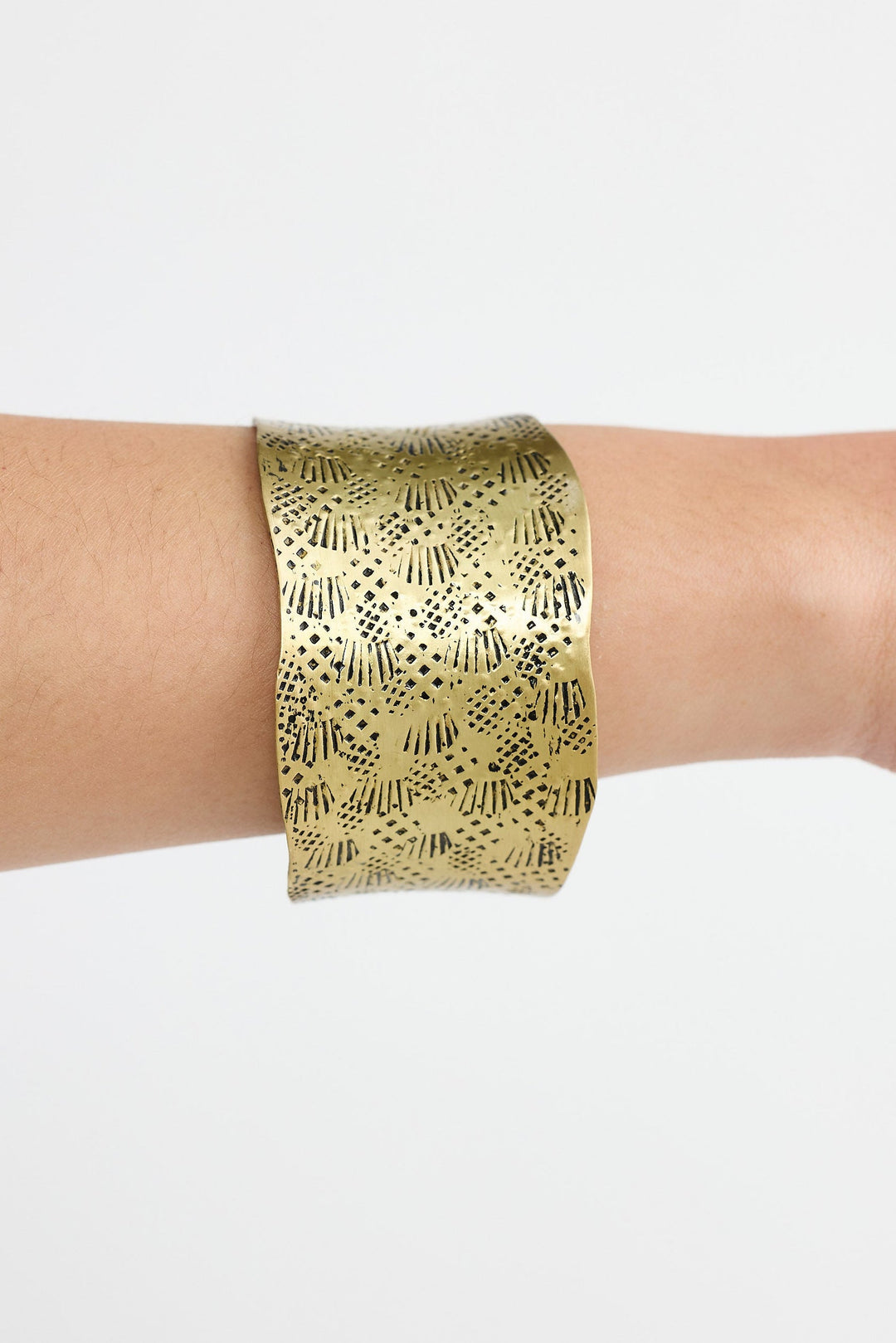 Gold bracelet with geometric pattern on a wrist against a white background