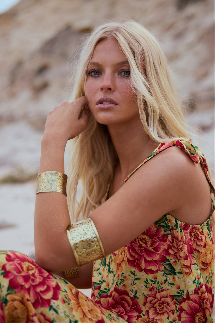 Woman in a floral dress with gold arm bands against a natural background