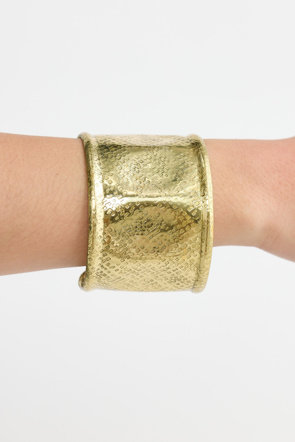 Gold cuff bracelet on a wrist against a white background