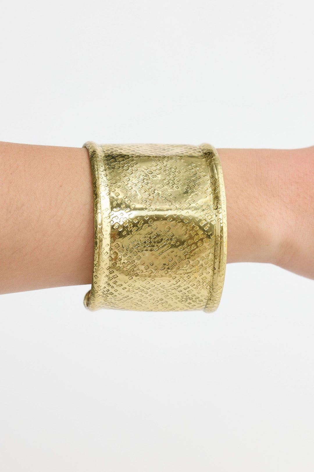 Gold cuff bracelet on a wrist against a white background