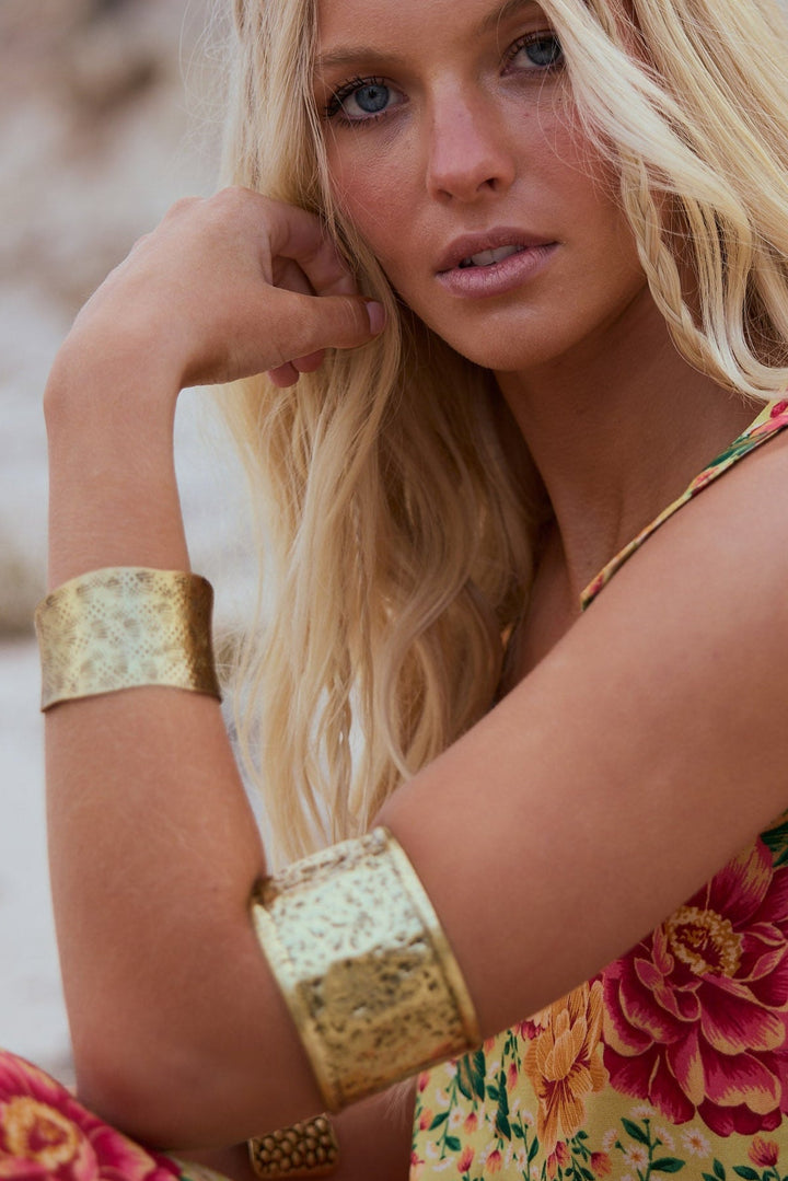 Woman in a floral dress with gold arm bands against a natural background