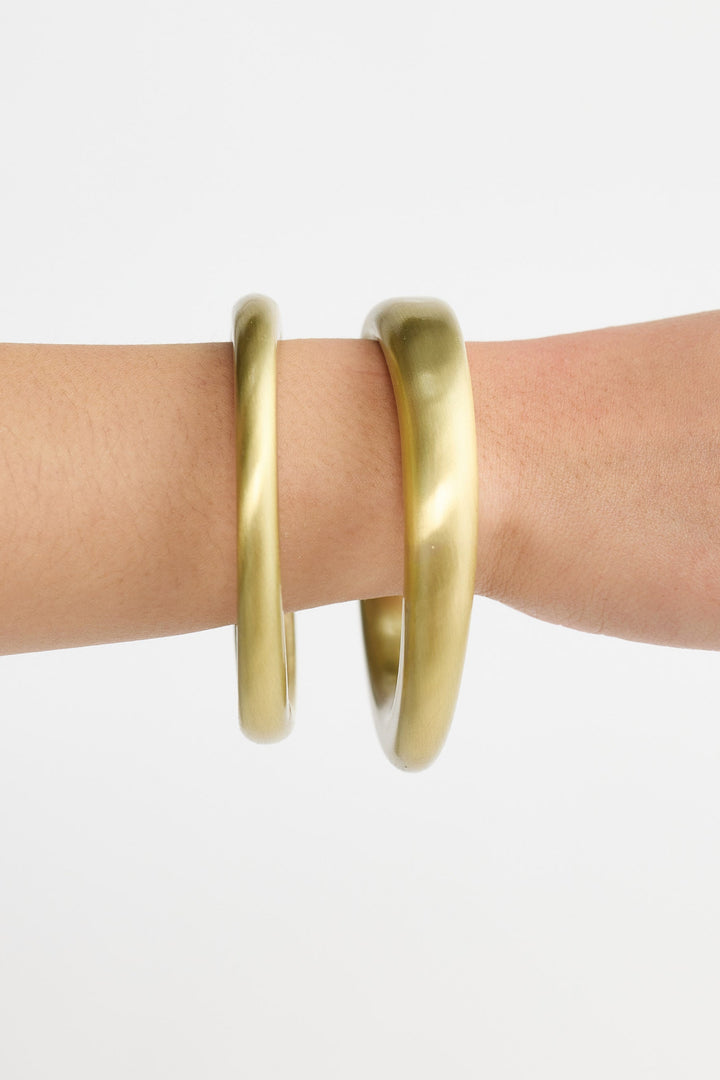 Gold bangles on a person's wrist against a white background