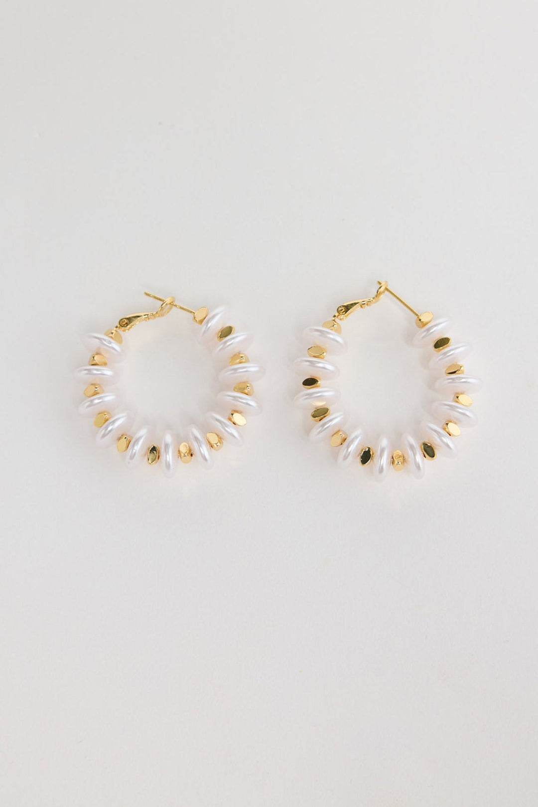 Pair of gold-tone hoop earrings made of stacked white pearl-look rondelle beads with small gold accents, laid flat on a white background