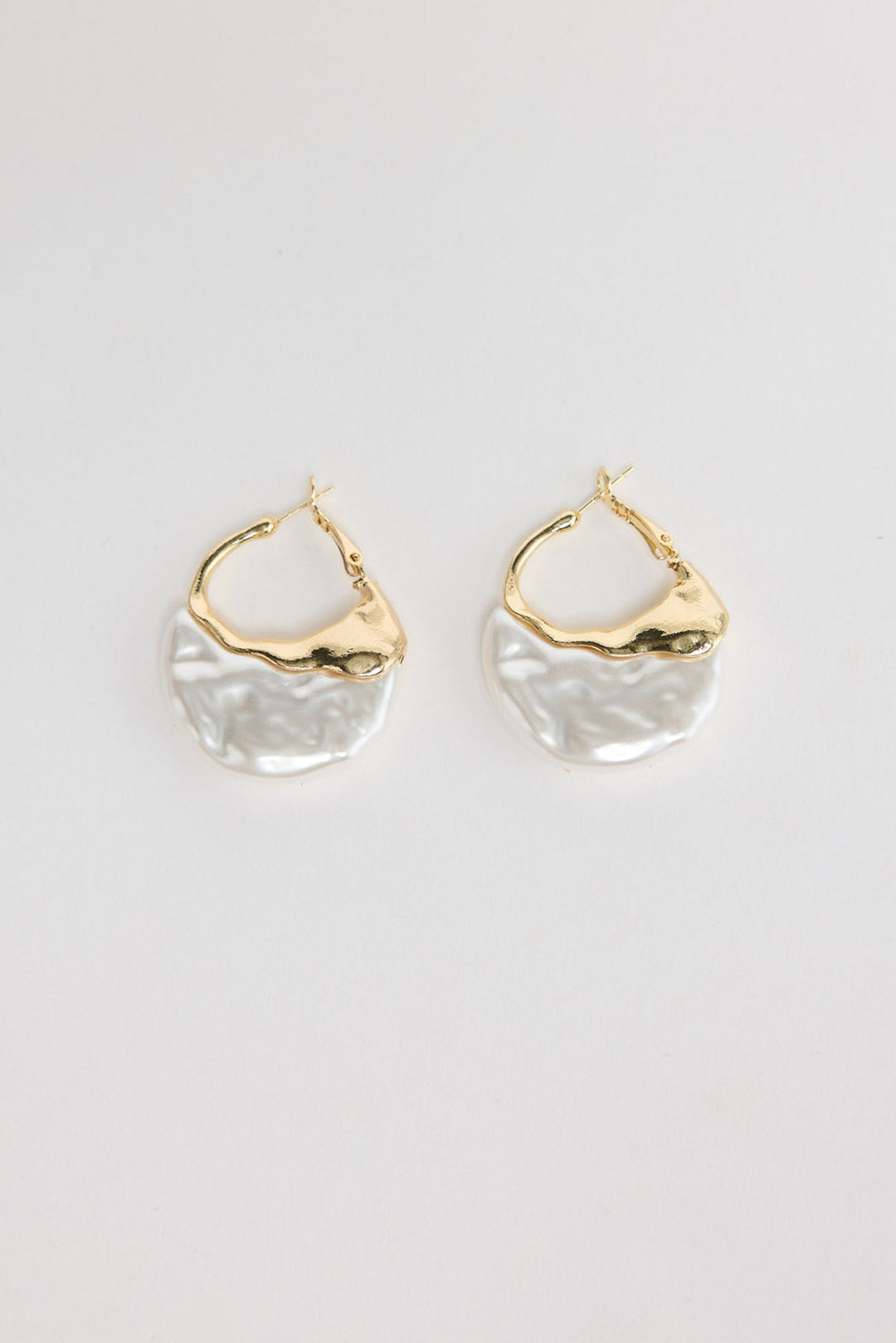 Pair of organic-shaped gold-tone hoop earrings with a textured white pearl-look resin drop, laid flat on a white background