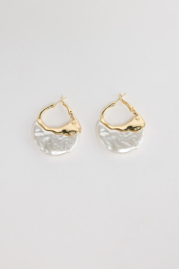 Pair of organic-shaped gold-tone hoop earrings with a textured white pearl-look resin drop, laid flat on a white background