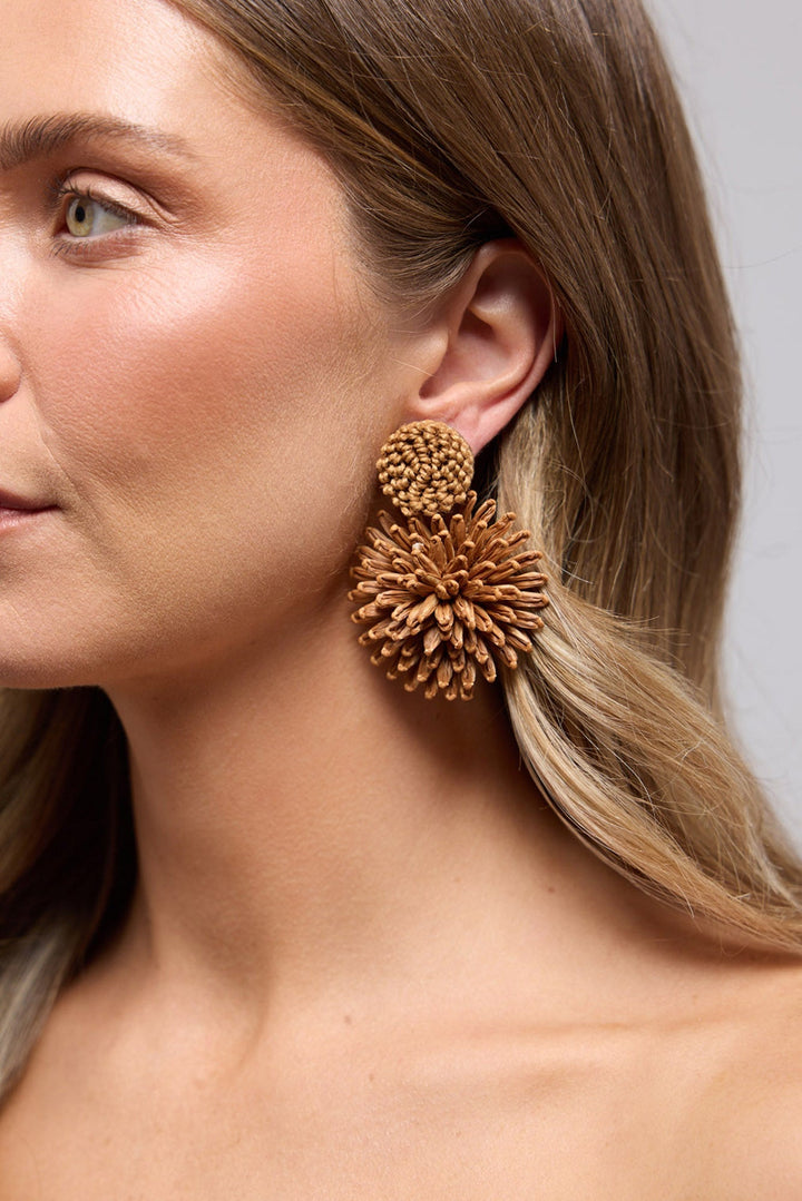 Polly statement earring in Tan worn on the ear, showing the woven raffia texture up close against the hair
