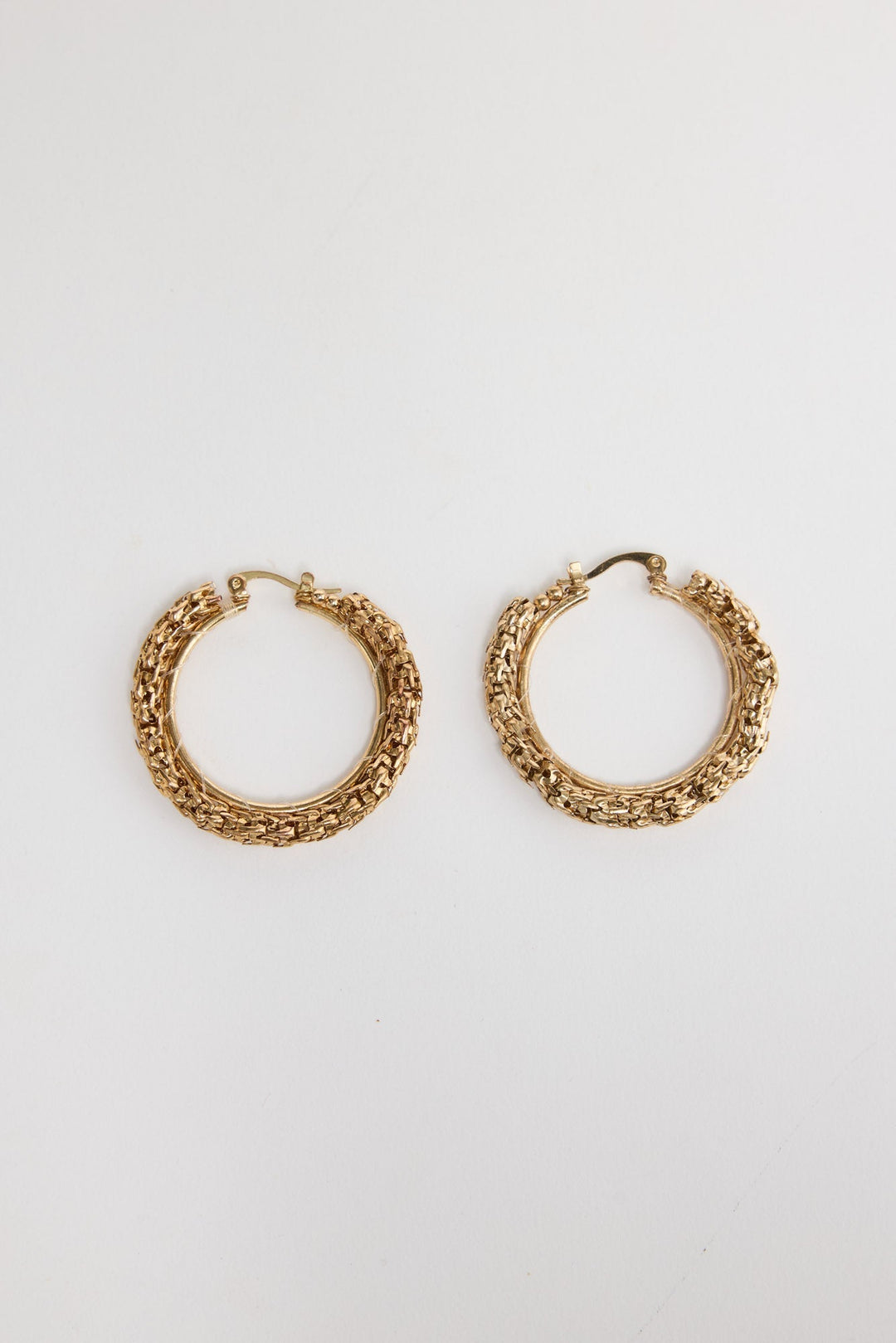 Pair of textured gold-tone Poppy hoop earrings laid flat, showing the woven metallic surface detail