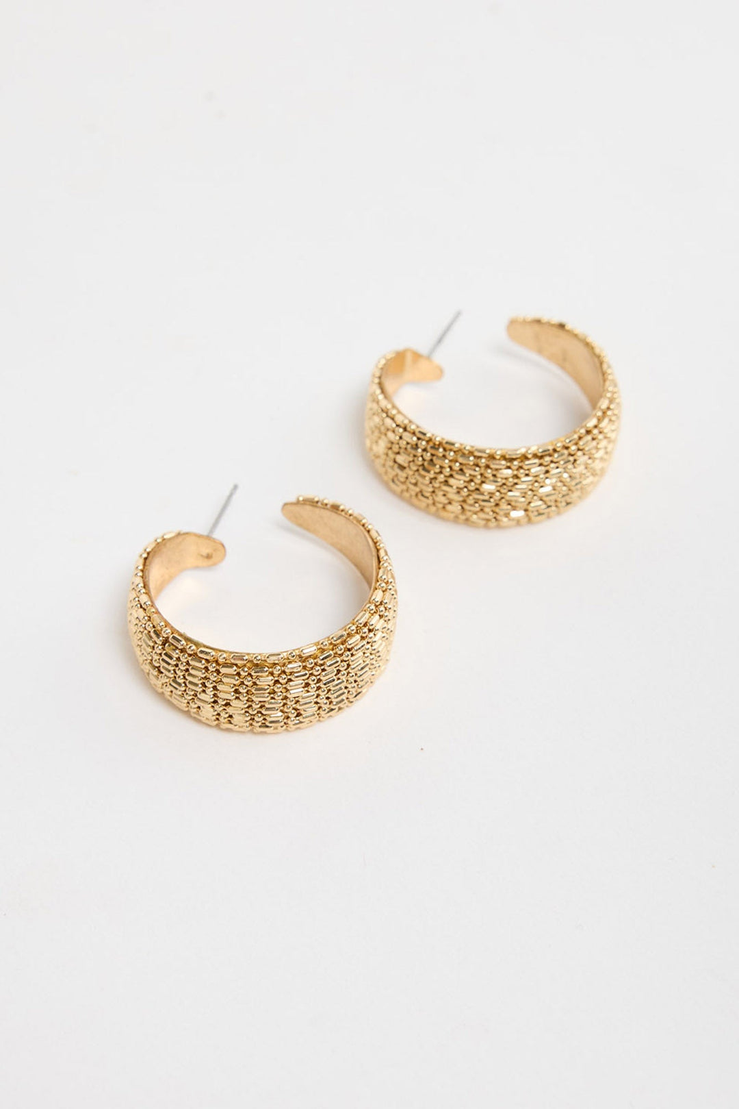 Pair of wide textured gold-tone Ione huggie earrings laid flat, showing the raised woven pattern