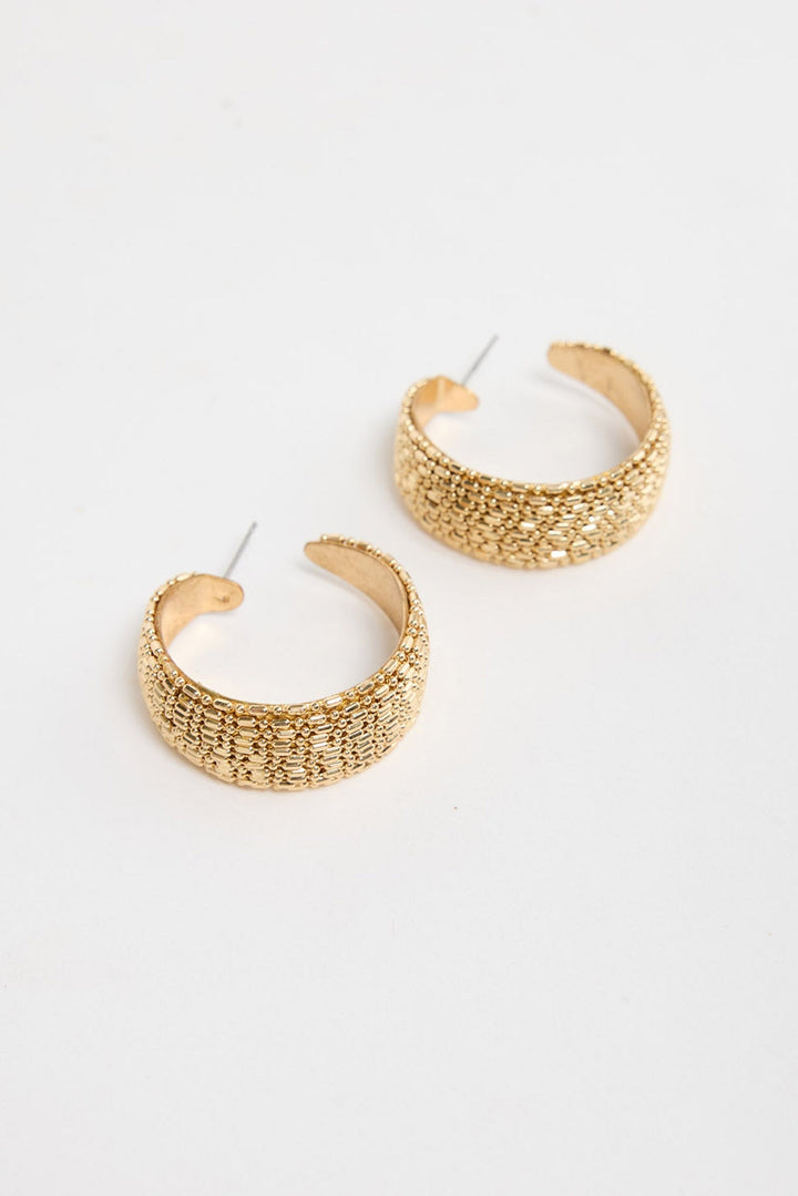 Pair of wide textured gold-tone Ione huggie earrings laid flat, showing the raised woven pattern