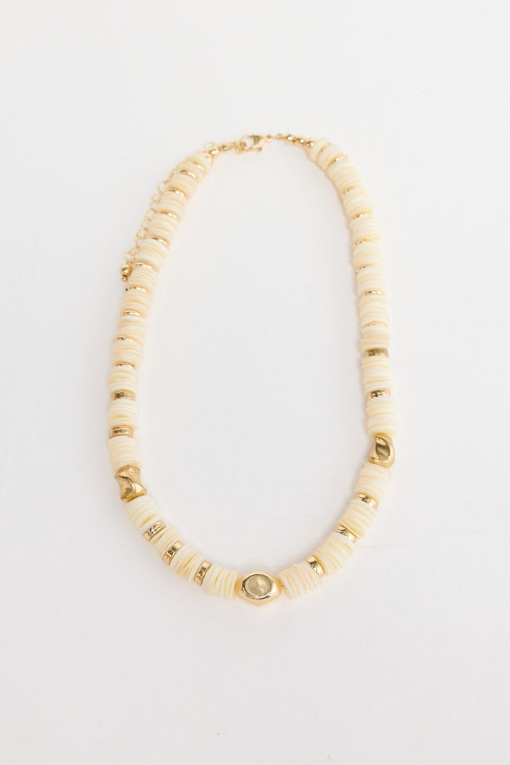 Cassian beaded necklace laid flat, showing cream disc beads interspersed with polished gold-tone accent beads