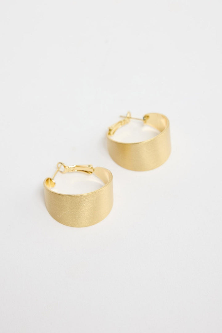 Siren Earrings in Gold worn on the ear, showing the wide hoop silhouette against the lobe.