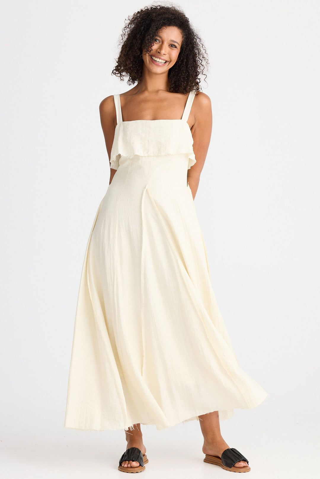 Woman wearing a cream dress with straps  and a ruffle on a white background