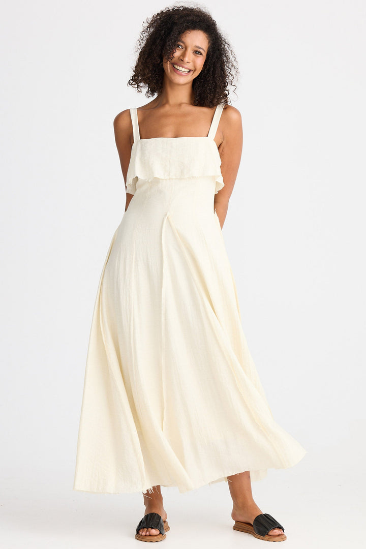 Woman wearing a cream dress with straps  and a ruffle on a white background