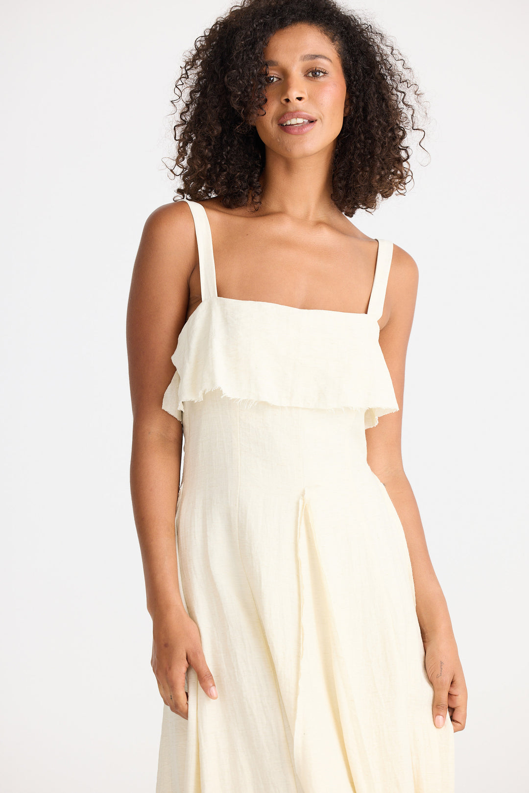 Woman wearing a cream dress with ruffled top on a white background