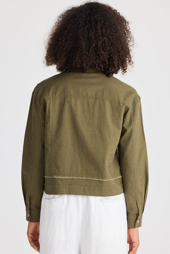 Person wearing an olive green jacket and white pants on a plain background