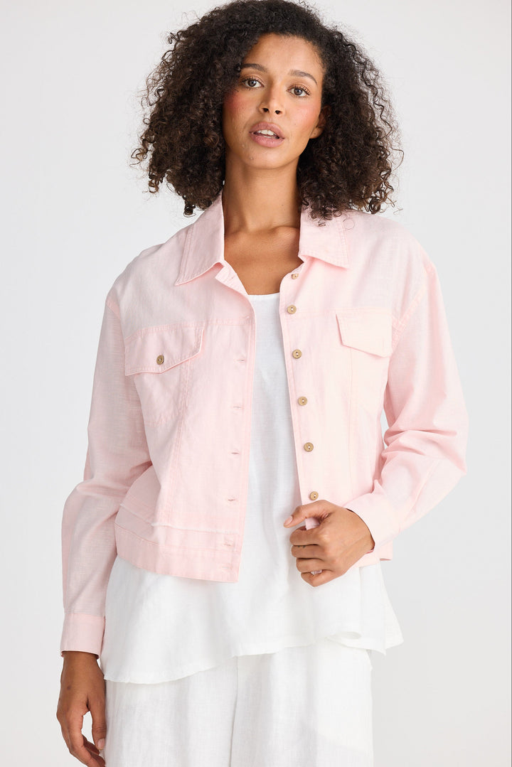 Woman wearing a light pink jacket over a white top on a plain background