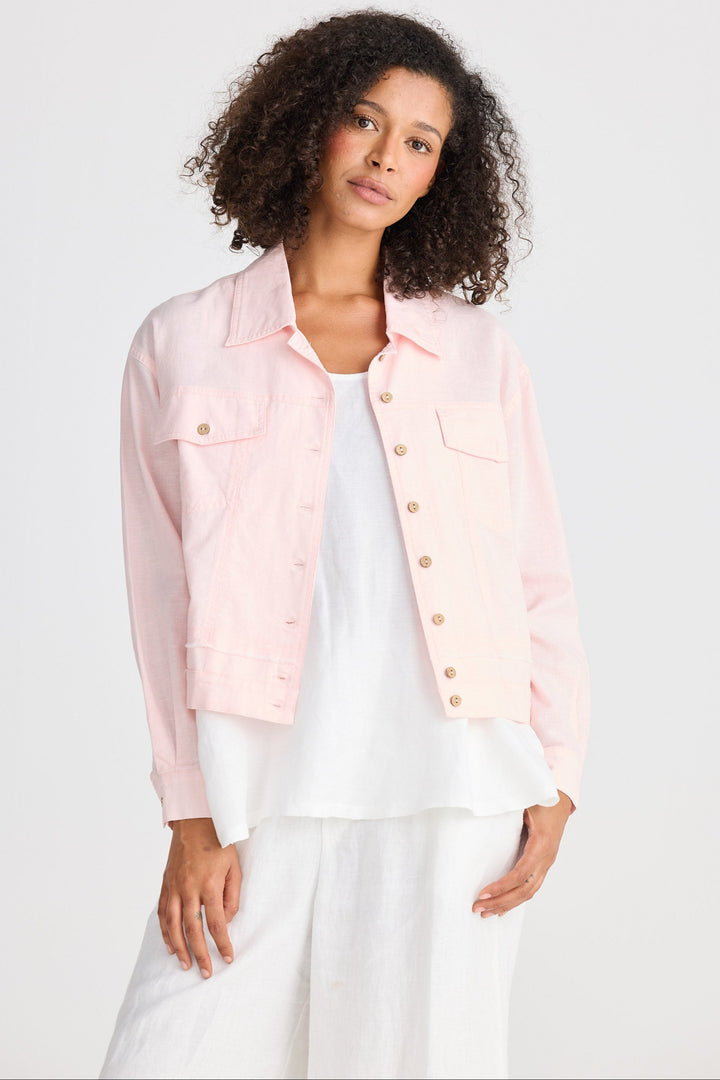 Woman wearing a light pink jacket over a white outfit on a plain background