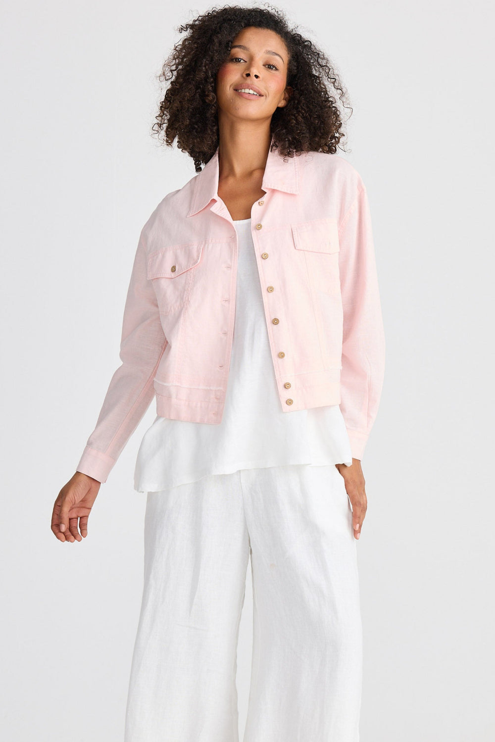 Woman wearing a light pink jacket over a white top and pants on a white background