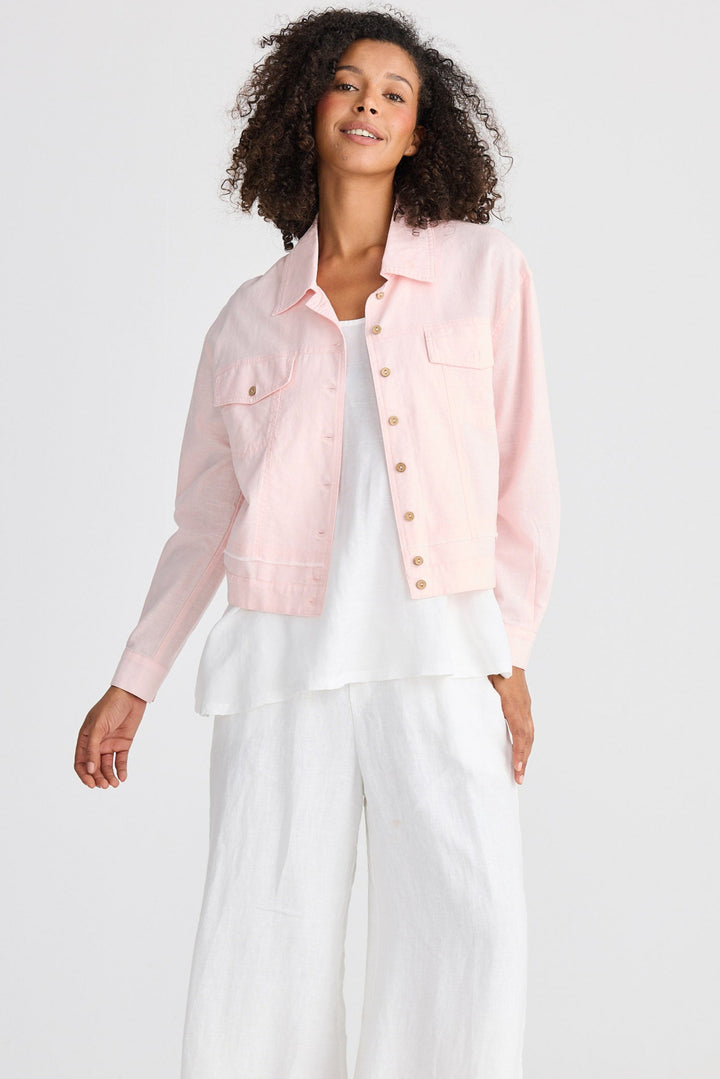 Woman wearing a light pink jacket over a white top and pants on a white background