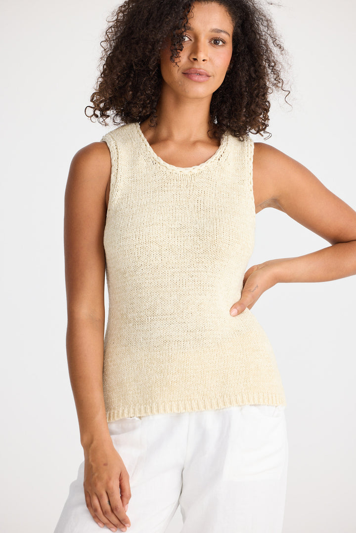 Woman wearing a natural sleeveless knitted top against a white background