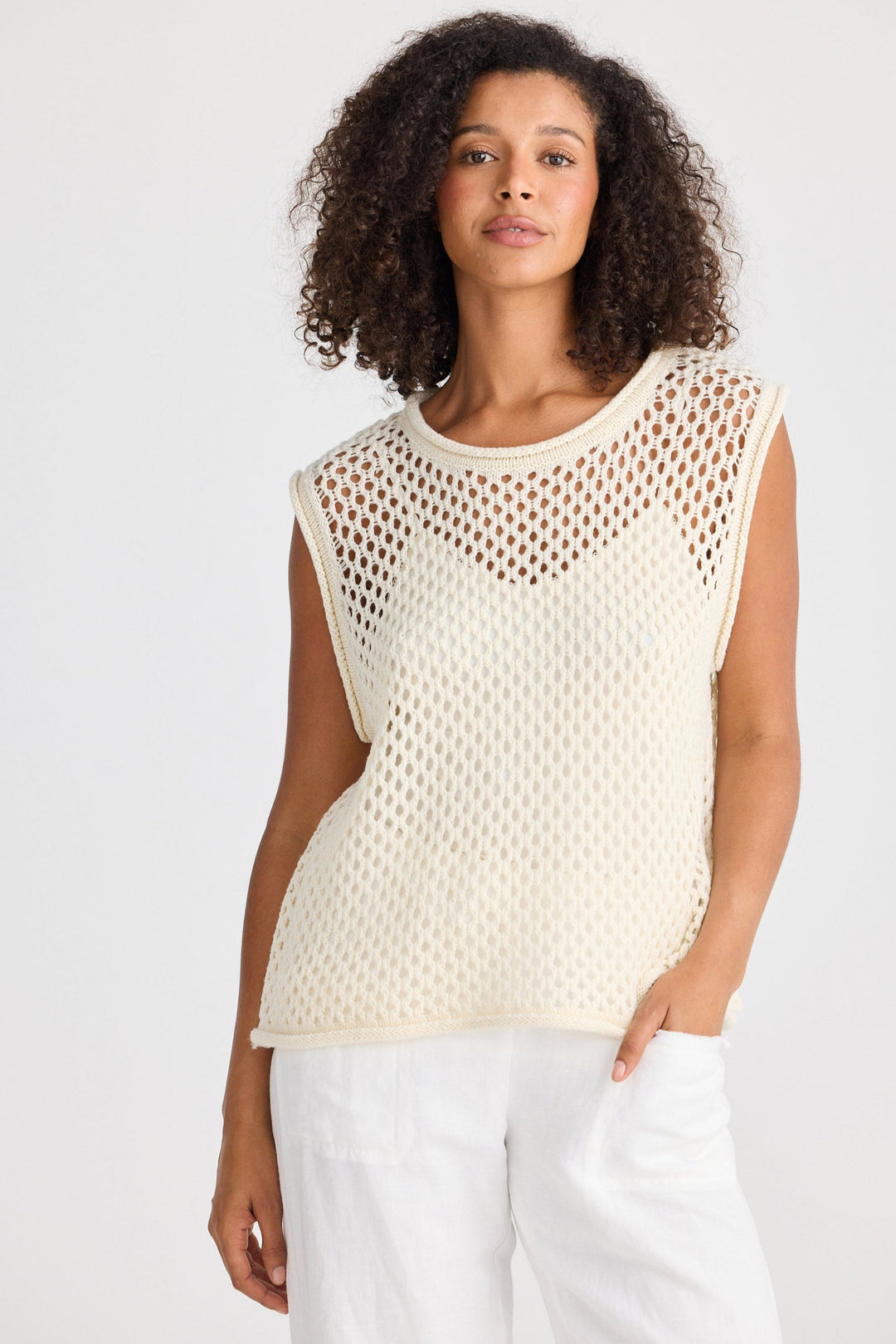 Woman wearing a beige mesh top and white pants on a plain background