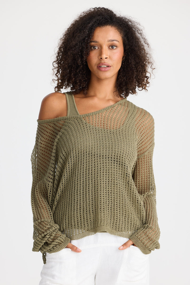 Woman wearing a green knit top with white pants on a white background