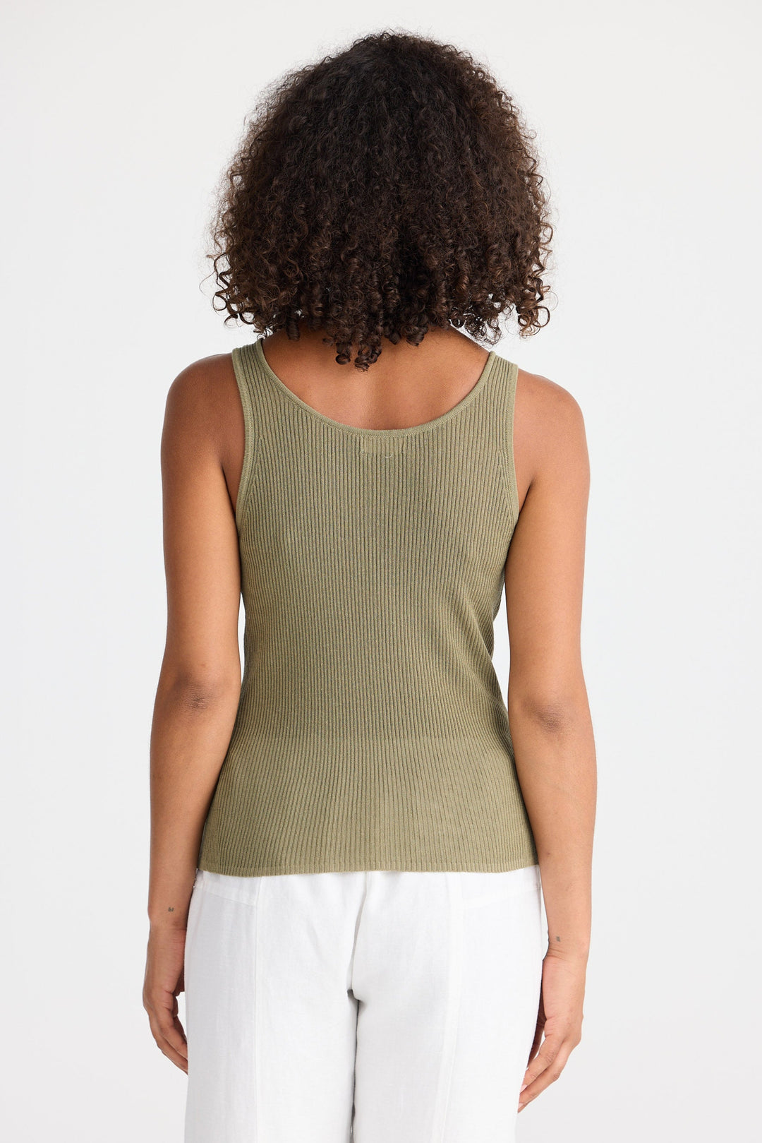 Woman wearing a green ribbed tank top and white pants on a white background