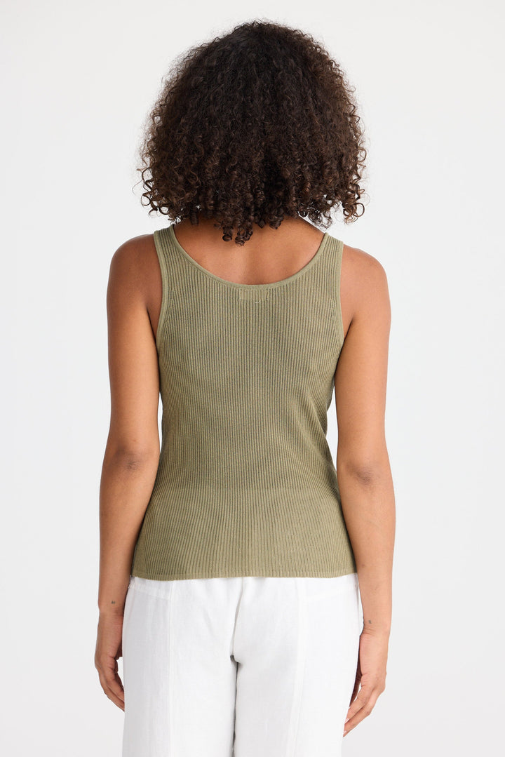 Woman wearing a green ribbed tank top and white pants on a white background