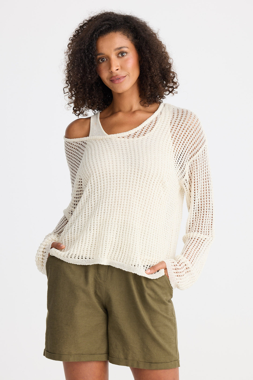 Woman wearing a cream knit sweater and green shorts on a plain background
