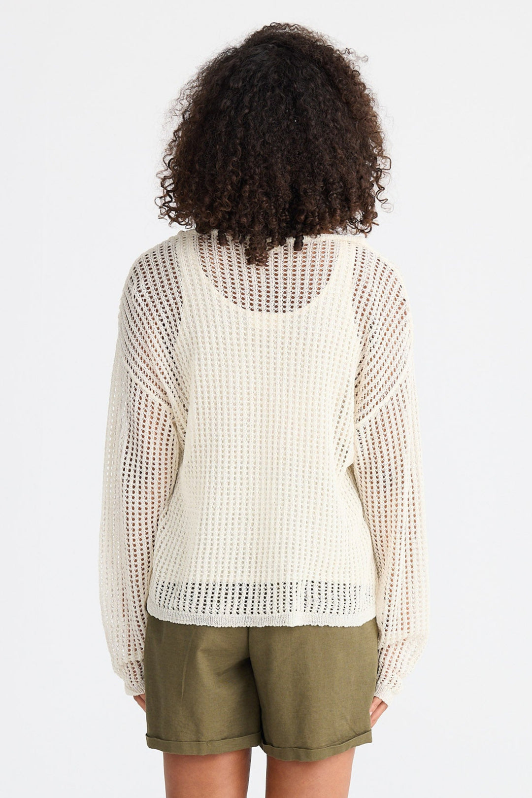 Person wearing a cream knit top and green shorts on a white background