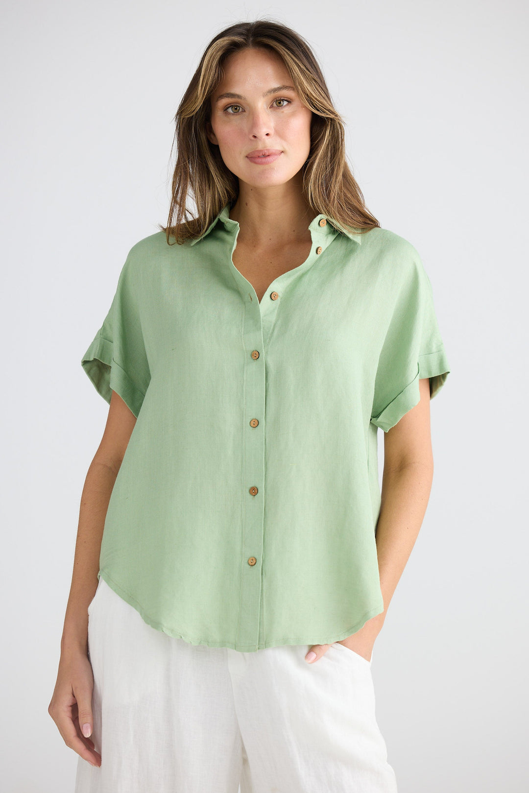 Woman wearing a light green button-up shirt with white pants on a plain background