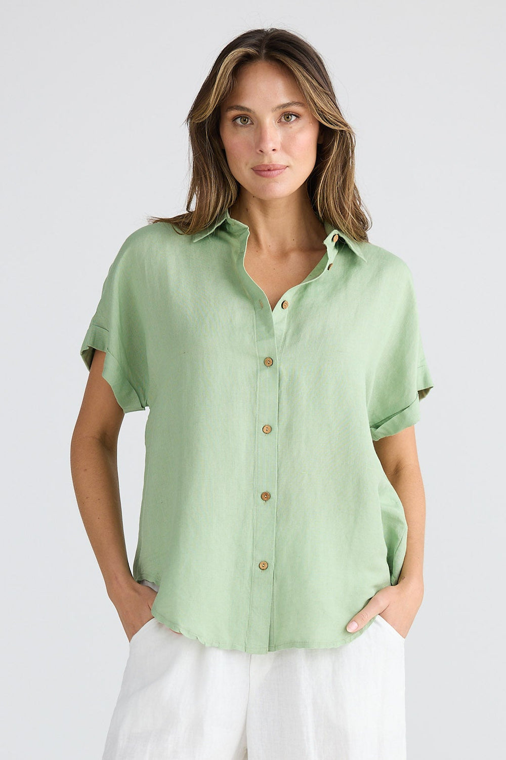 Woman wearing a light green shirt and white pants on a plain background