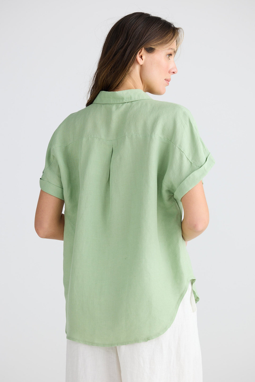 Woman wearing a light green shirt and white pants on a plain background