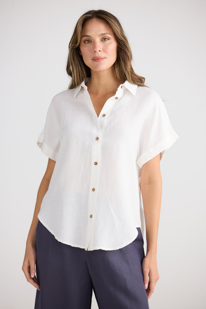 Woman wearing a white shirt with short sleeves and navy pants on a plain background